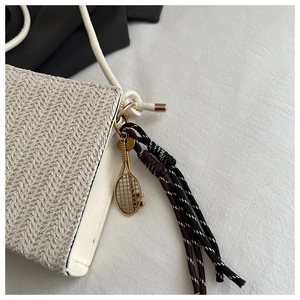 Detail of straw tote bag featuring gold tennis racket charm and striped tassel fringe
