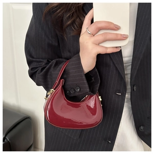 Close-up of minimalist burgundy patent leather crescent underarm bag with gold metal buckle
