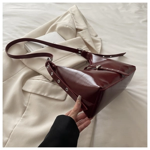 Détail du sac bandoulière en cuir verni bordeaux avec oeillets argentés et boucle