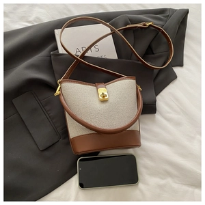 Detail shot of a two-tone canvas bucket bag with brown leather trim and gold hardware