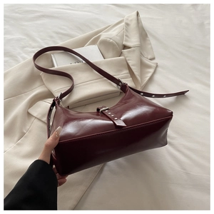 Détail du sac sous l'aisselle bordeaux avec boucle argentée sur fond beige épuré