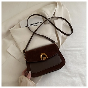 Close-up of dark brown suede crossbody bag with golden horseshoe buckle on beige blazer