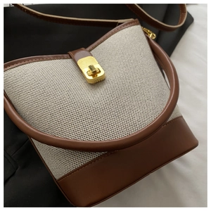 Detail of canvas bucket bag showing leather trim and gold twist-lock closure