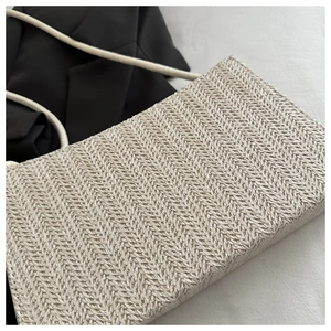 Detail of a beige woven straw tote bag with herringbone pattern on black and white fabric