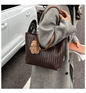 Detail of dark brown woven tote bag with wide leather strap and plush bear charm
