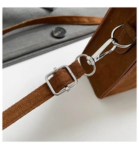 Detail of brown suede handbag featuring adjustable strap with silver square metal buckle