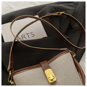Close-up of beige woven canvas bucket bag with brown leather trim and golden metal clasp