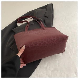 Detail of burgundy tote bag featuring subtle leopard texture and leather straps