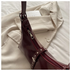 Détail d'un sac à bandoulière en cuir verni bordeaux avec rivets sur costume crème