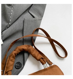 Macro view of brown suede handbag with pleated handle and thin strap on grey blazer