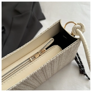 Detail of beige straw tote bag with black fabric lining, gold ring, and zipper closure