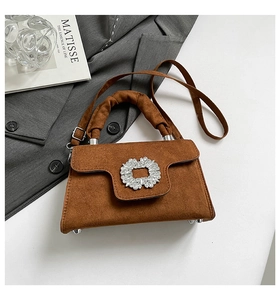Detail of a brown suede handbag featuring a crystal buckle and pleated handle texture
