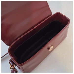 Detail view of burgundy glossy shoulder bag with gold magnetic closure and interior space
