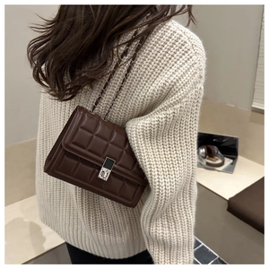 Detail of dark brown quilted crossbody bag with silver chain strap and metal turn-lock