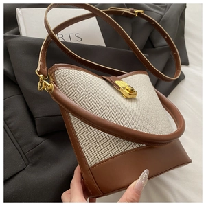 Detail of canvas bucket bag showing gold metal swivel lock and brown leather strap