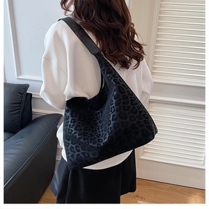 Close-up of black leopard print hobo tote bag with wide shoulder strap on a model