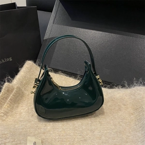 Glossy deep green patent leather hobo bag with gold hardware on a beige knit background