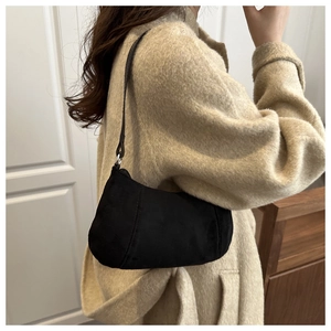 Side view of a black suede baguette bag worn with a beige wool coat for fall fashion