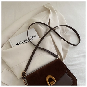 Detail of dark brown crossbody bag with gold horseshoe buckle on a white blazer