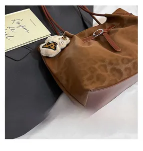 Detail of leopard print suede tote with leather handles and a plush character charm