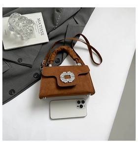 Detail of a brown suede handbag featuring a luxury square crystal buckle and pleated handle