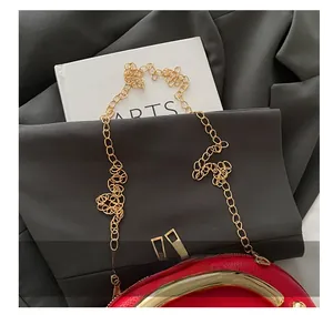 Detail of red pebbled leather handbag with gold arc handle and fine chain strap