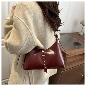 Détail du sac hobo bordeaux brillant avec boucle à rivets argentés sur fond de manteau