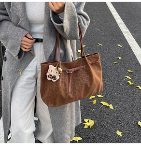 Outdoor view of a vintage leopard embossed tote bag with plush charm on a grey coat