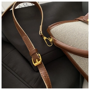 Detail of adjustable brown leather strap and gold-tone metal hardware on woven bucket bag
