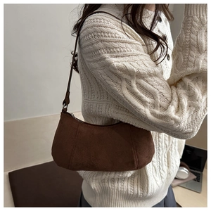 Brown faux suede baguette bag worn on shoulder with cream knit sweater detail