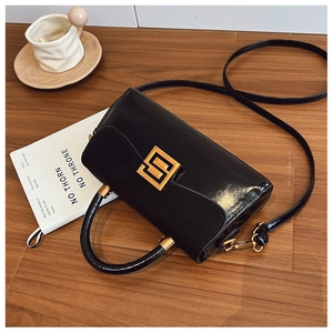 Detail of a vintage black matte leather handbag with gold metal clasp on a wooden table