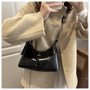Gros plan d'un sac en cuir verni noir avec boucle argentée et rivets sur manteau beige