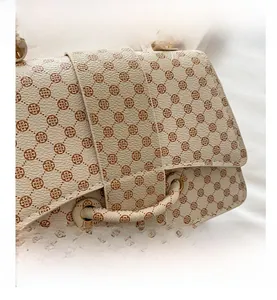 Detail of cream faux leather handbag with brown floral patterns and metal eyelets