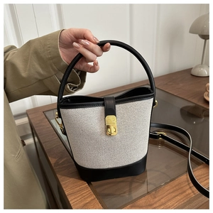 Detail of canvas bucket bag with black leather trim and gold metal clasp closure