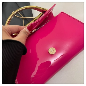 Close-up of fuchsia patent leather handbag with gold metal handle and magnetic clasp