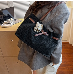Detail of leopard print tote bag featuring brown leather straps and plush charm accessory