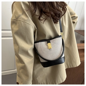 Detail of canvas bucket bag with black leather trim and gold metal rotating buckle
