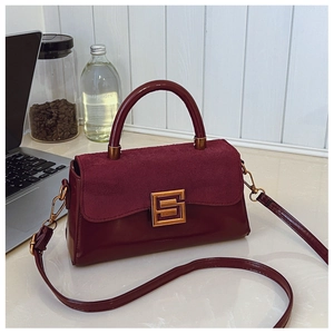 Detail of burgundy patchwork handbag with suede flap and gold buckle on a desk