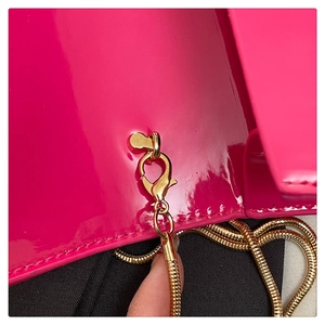 Close-up of bright pink patent leather bag with gold metal chain and stitching details