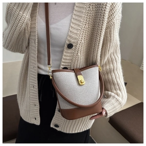 Detail of a two-tone bucket bag with beige canvas, brown leather trim, and gold clasp
