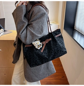 Close-up of leopard print tote bag with brown leather handles and a cat charm detail