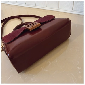Detail of dark burgundy crossbody bag showing textured leather and vintage metal buckle