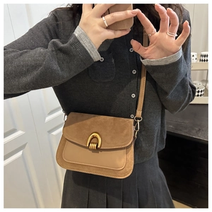 Close-up of brown leather bag featuring a stylish gold horseshoe buckle and mixed textures