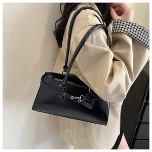 Détail d'un sac sous le bras en cuir verni noir avec boucle argentée sur modèle