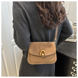 Detail of a brown leather crossbody bag with suede flap and vintage gold horseshoe lock