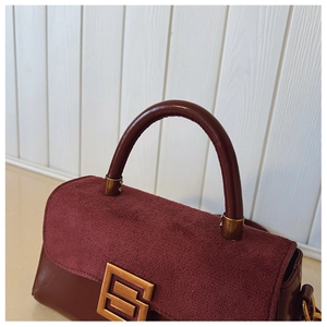 Close-up of deep burgundy leather and suede stitching with a gold geometric buckle