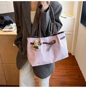 Detail of light pink nylon tote bag featuring brown leather handles and belt buckle accent