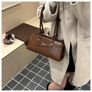 Gros plan d'un sac baguette en cuir marron avec de fines lanières sur un manteau