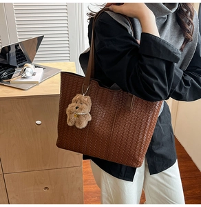 Detail of deep brown woven tote bag featuring a cute plush dog pendant and herringbone pattern