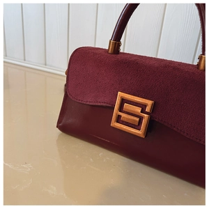 Detail of burgundy crossbody bag featuring suede flap and smooth leather texture